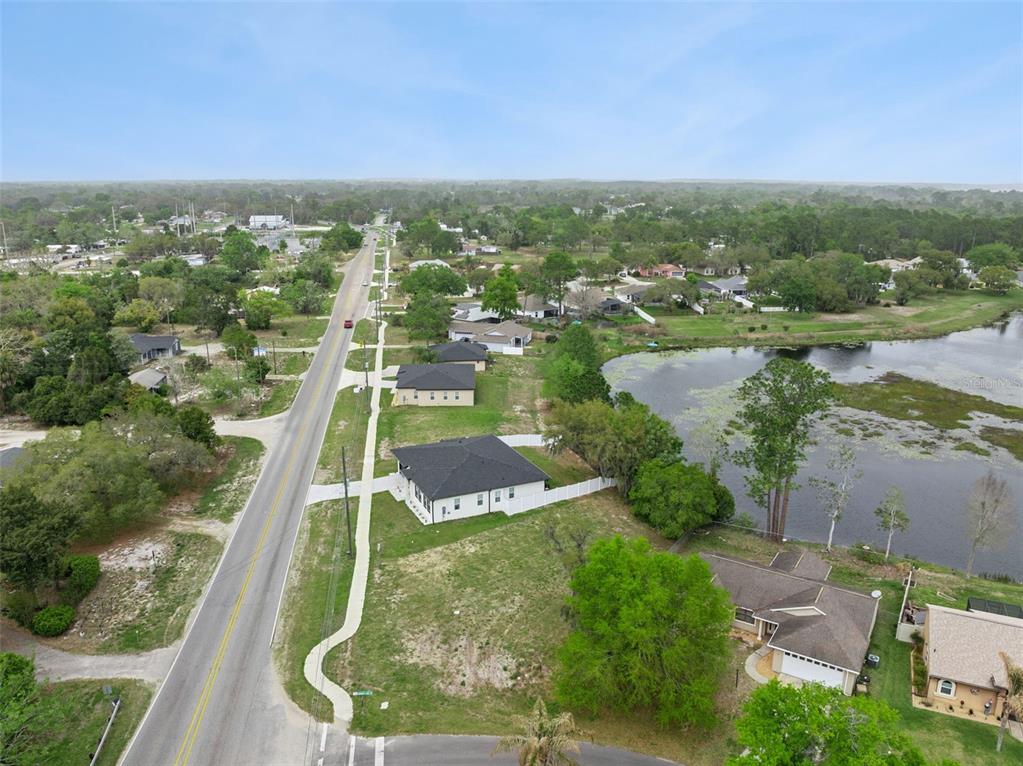 An aerial view shows a suburban street with houses, a lake, and surrounding greenery — COUNTY ROAD 473, LEESBURG, FL