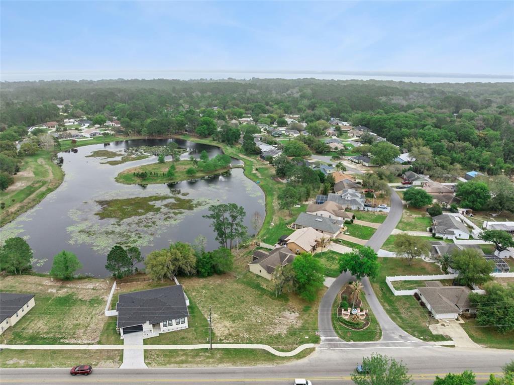 An aerial view shows a suburban neighborhood with houses surrounding a large pond — COUNTY ROAD 473, LEESBURG, FL
