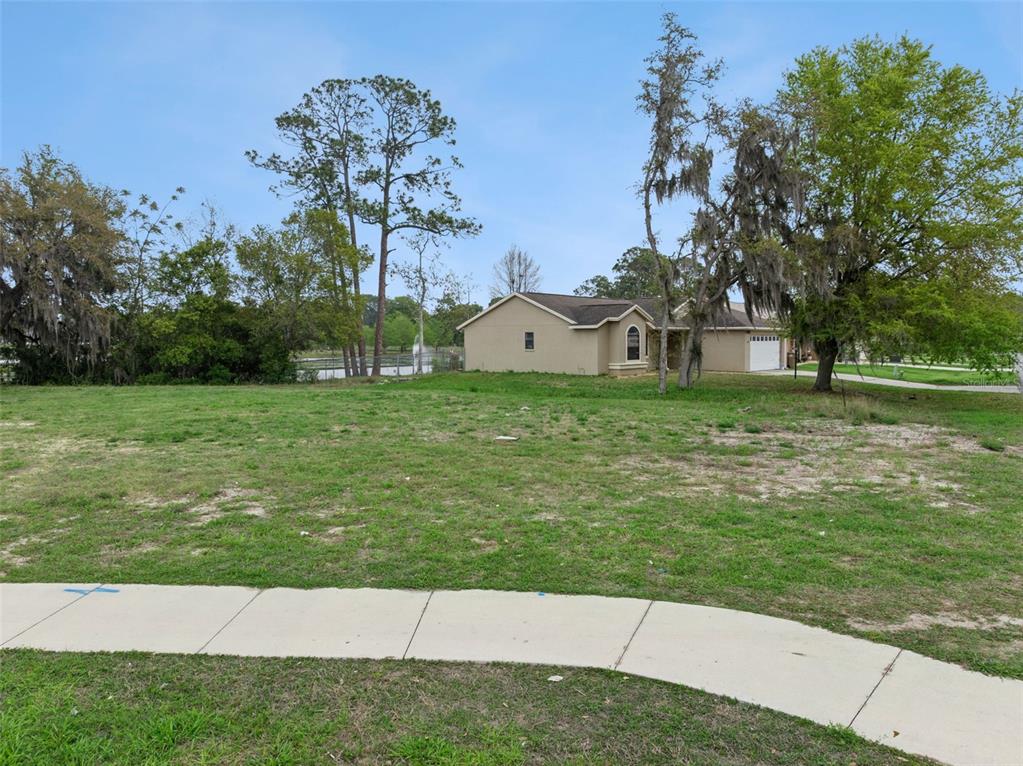 A vacant grassy lot sits in front of a tan single-story house with trees — COUNTY ROAD 473, LEESBURG, FL