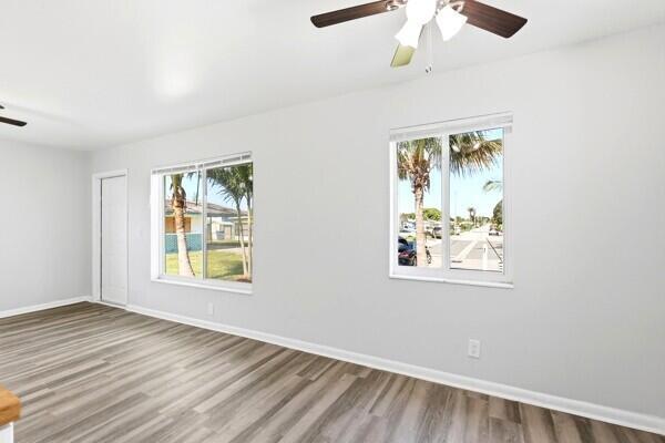 A bright, empty room features light gray walls, wood-look flooring, two windows, and a ceiling fan — 2302 Avenue M, Riviera Beach FL 33404, RIVIERA BEACH, FL