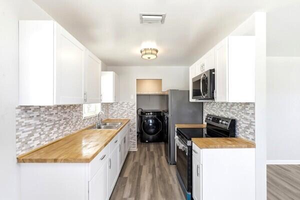 A kitchen features white cabinets, butcher block countertops, a tiled backsplash, and stainless steel appliances — 2302 Avenue M, Riviera Beach FL 33404, RIVIERA BEACH, FL
