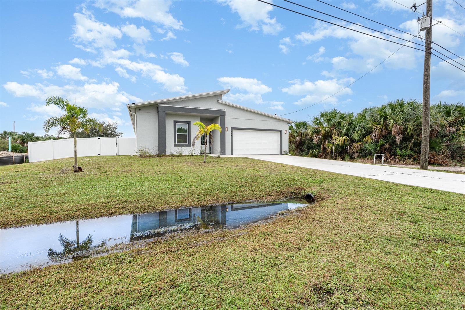 A single-story house with a white garage and a small pond in the front yard — 448 Saint Andre Boulevard, Palm Bay FL 32908, PALM BAY, FL