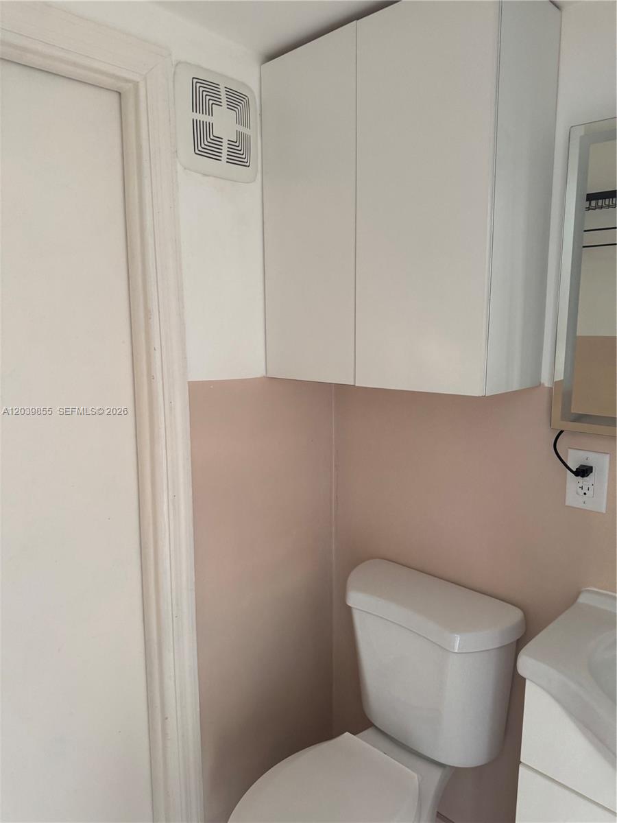 A bathroom features a white toilet, a wall-mounted cabinet, and a vent on the wall — MIAMI GARDENS, FL