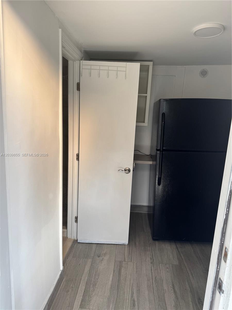 A kitchen features a black refrigerator, light wood-look flooring, and a white door — MIAMI GARDENS, FL