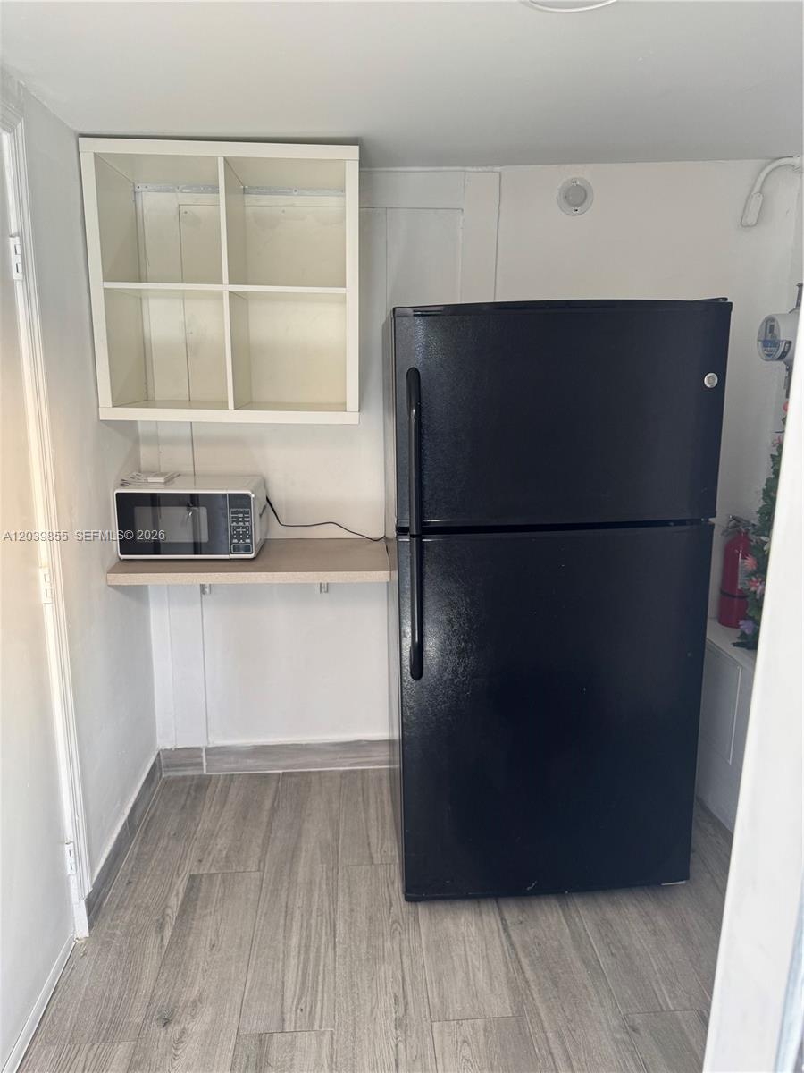 A small kitchen area features a black refrigerator, a microwave on a shelf, and wood-look flooring — MIAMI GARDENS, FL