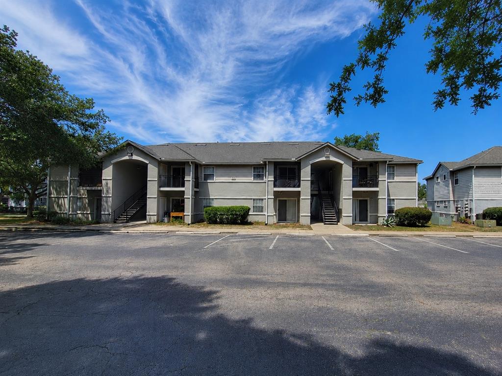 A two-story apartment building with a parking lot in the foreground under a blue sky — 3705 SW 27TH STREET UNIT 818, GAINESVILLE, FL