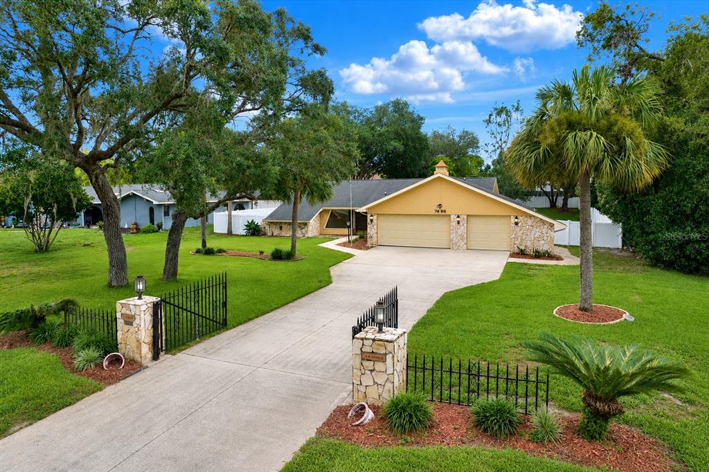 A single-story house with a two-car garage and stone accents sits behind a gated driveway — 7488 RIVER COUNTRY DRIVE, WEEKI WACHEE, FL