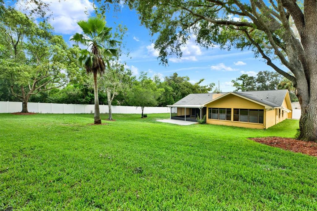A yellow house with a screened-in patio sits on a large, grassy backyard lot — 7488 RIVER COUNTRY DRIVE, WEEKI WACHEE, FL