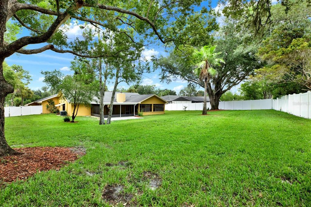 A yellow house with a screened porch sits in a large, grassy backyard with trees — 7488 RIVER COUNTRY DRIVE, WEEKI WACHEE, FL