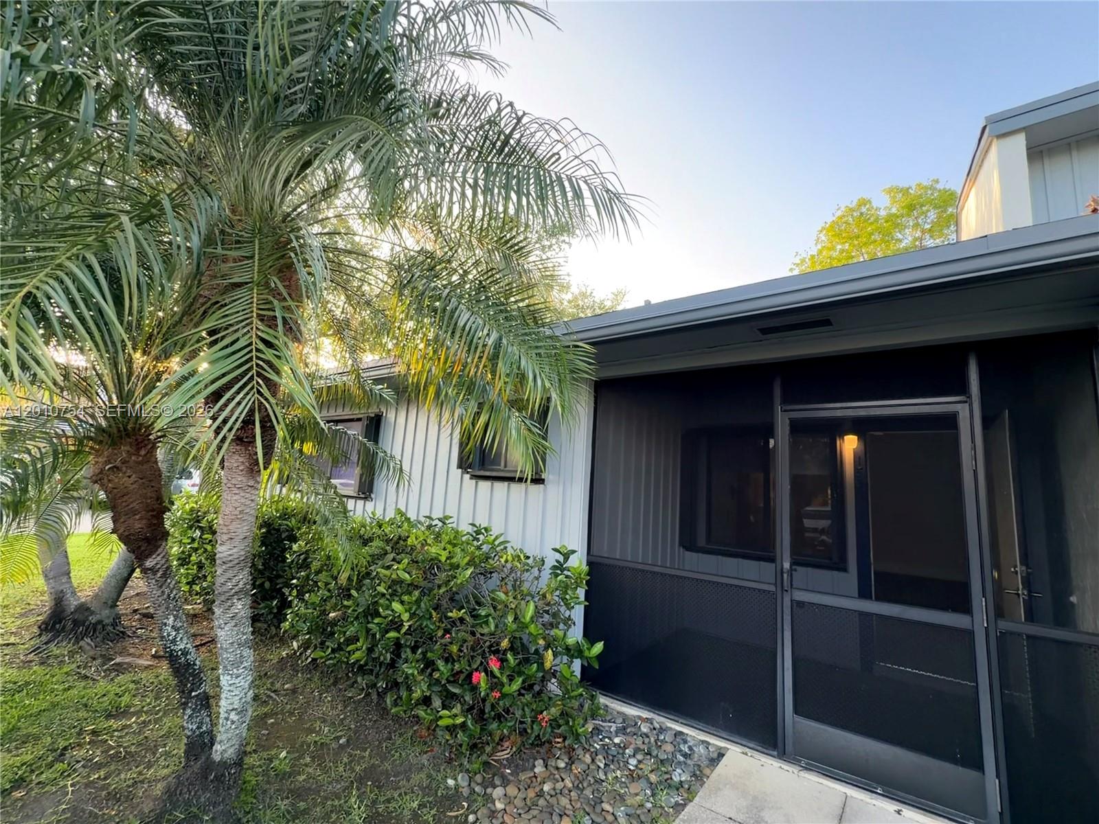 A palm tree stands beside a house with a screened-in porch and light-colored siding — 1533 Gabriel St, Hollywood FL 33020, HOLLYWOOD, FL