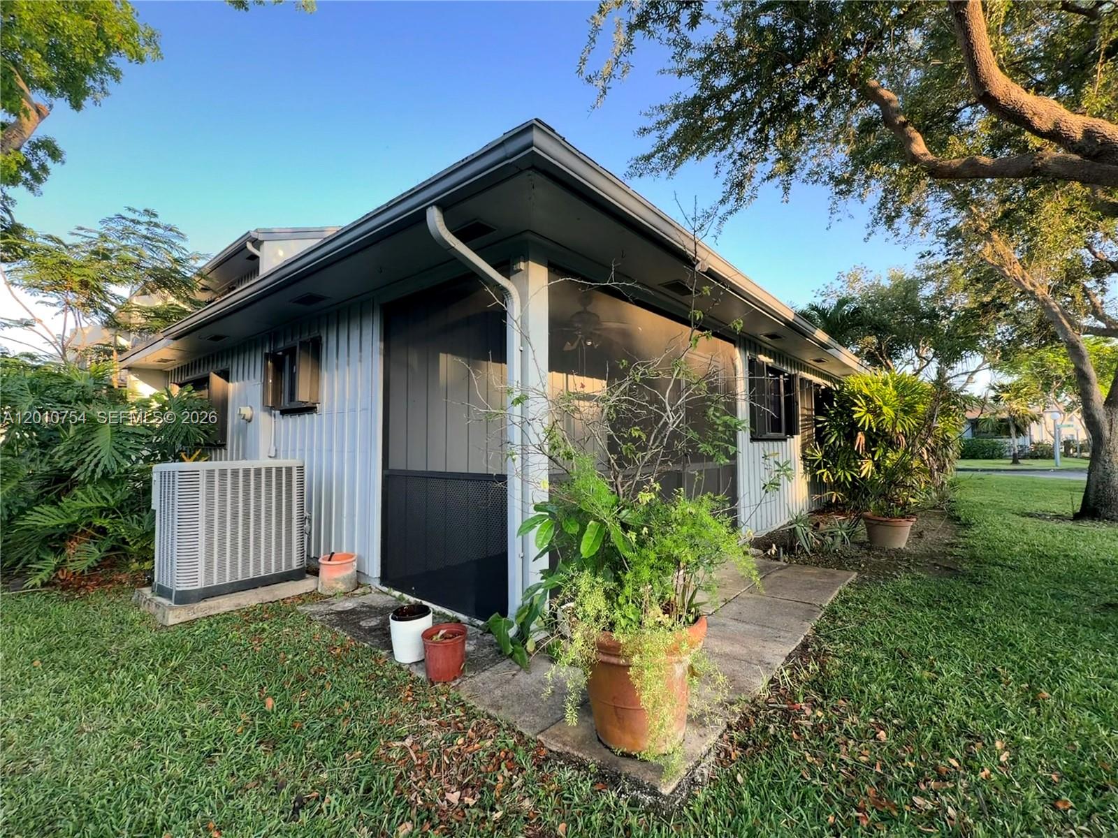 The exterior of a light-colored house features a screened-in porch, an AC unit, and landscaping — 1533 Gabriel St, Hollywood FL 33020, HOLLYWOOD, FL