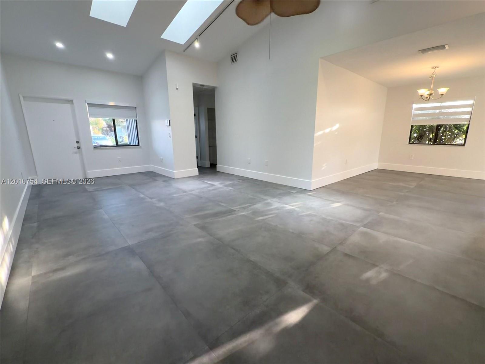 A bright, open-concept living area features large gray floor tiles, white walls, and skylights — 1533 Gabriel St, Hollywood FL 33020, HOLLYWOOD, FL