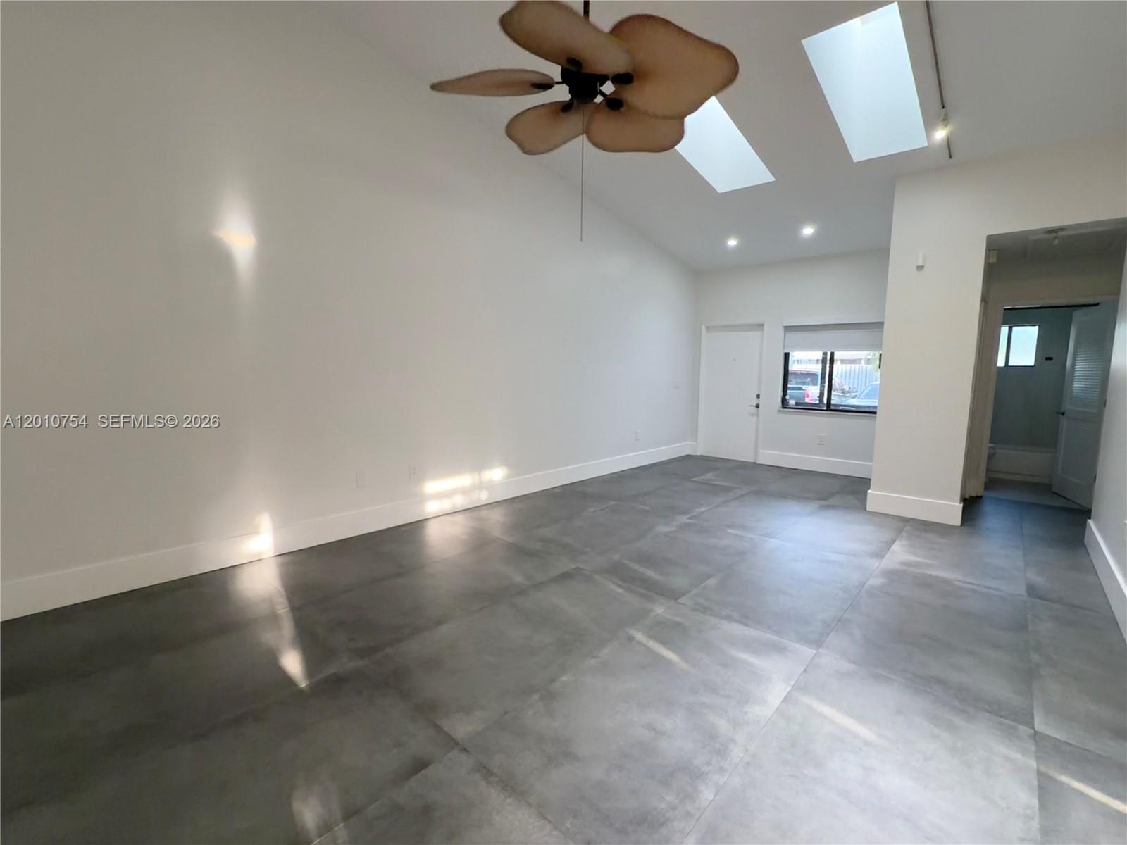A bright, empty room features large gray floor tiles, a vaulted ceiling, and skylights — 1533 Gabriel St, Hollywood FL 33020, HOLLYWOOD, FL