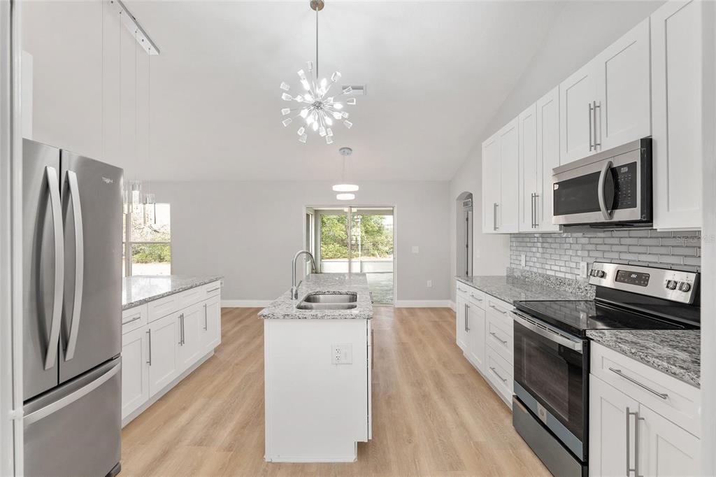 A modern kitchen features white cabinets, granite countertops, a center island, and stainless steel appliances — 4181 SW 111TH PLACE, OCALA, FL