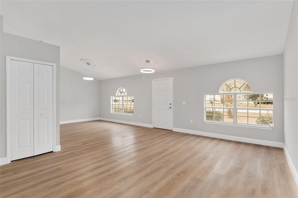 An empty living room features light gray walls, wood-look flooring, two windows, and white doors — 4181 SW 111TH PLACE, OCALA, FL