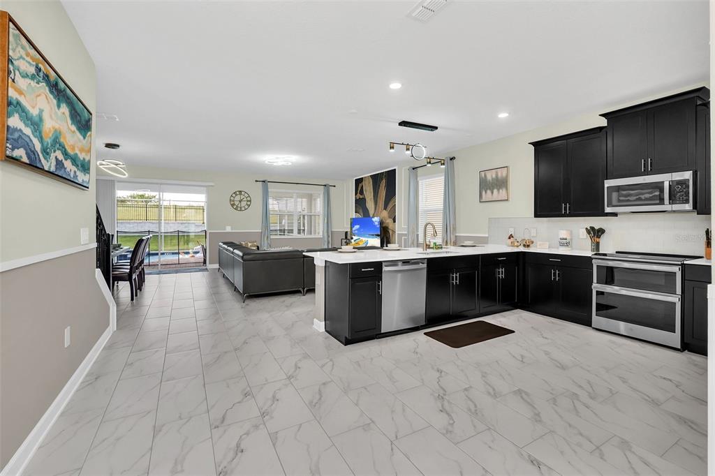 An open-concept kitchen with dark cabinets and a large island overlooks a living area — 9194 SOMMERSET HILLS DRIVE, DAVENPORT, FL