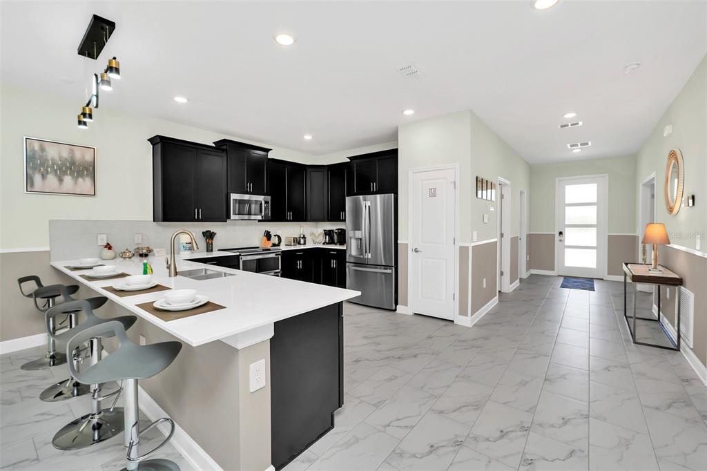 A modern kitchen features dark cabinetry, a white quartz island with bar seating, and tile flooring — 9194 SOMMERSET HILLS DRIVE, DAVENPORT, FL