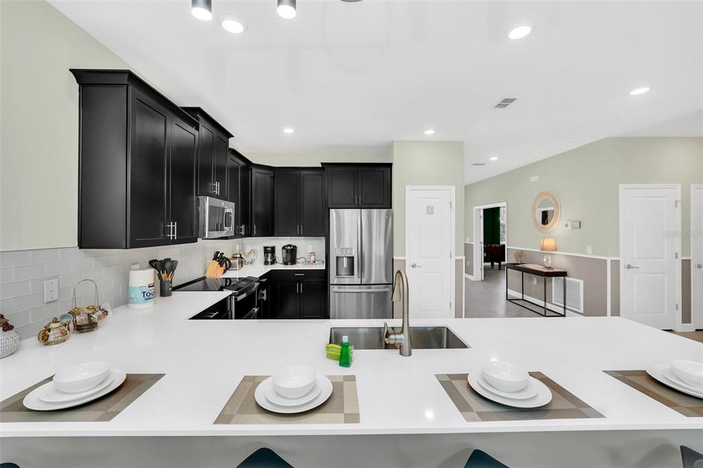 A kitchen features black cabinets, white countertops, stainless steel appliances, and a breakfast bar — 9194 SOMMERSET HILLS DRIVE, DAVENPORT, FL