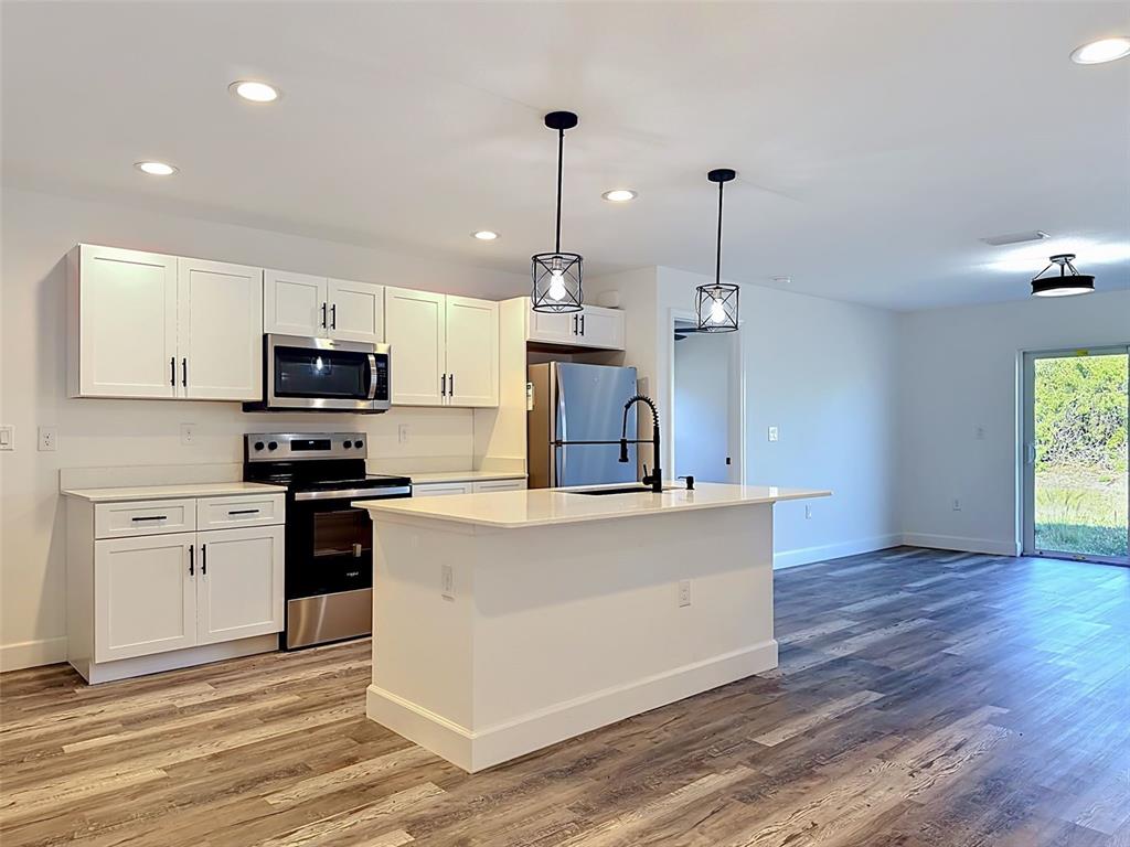 A modern kitchen features white cabinets, stainless steel appliances, a center island, and wood-look flooring — 2715 GISELA RD, NORTH PORT, FL