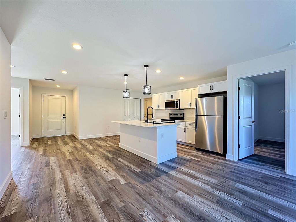 A kitchen with white cabinets, a central island, and stainless steel appliances over wood flooring — 2715 GISELA RD, NORTH PORT, FL