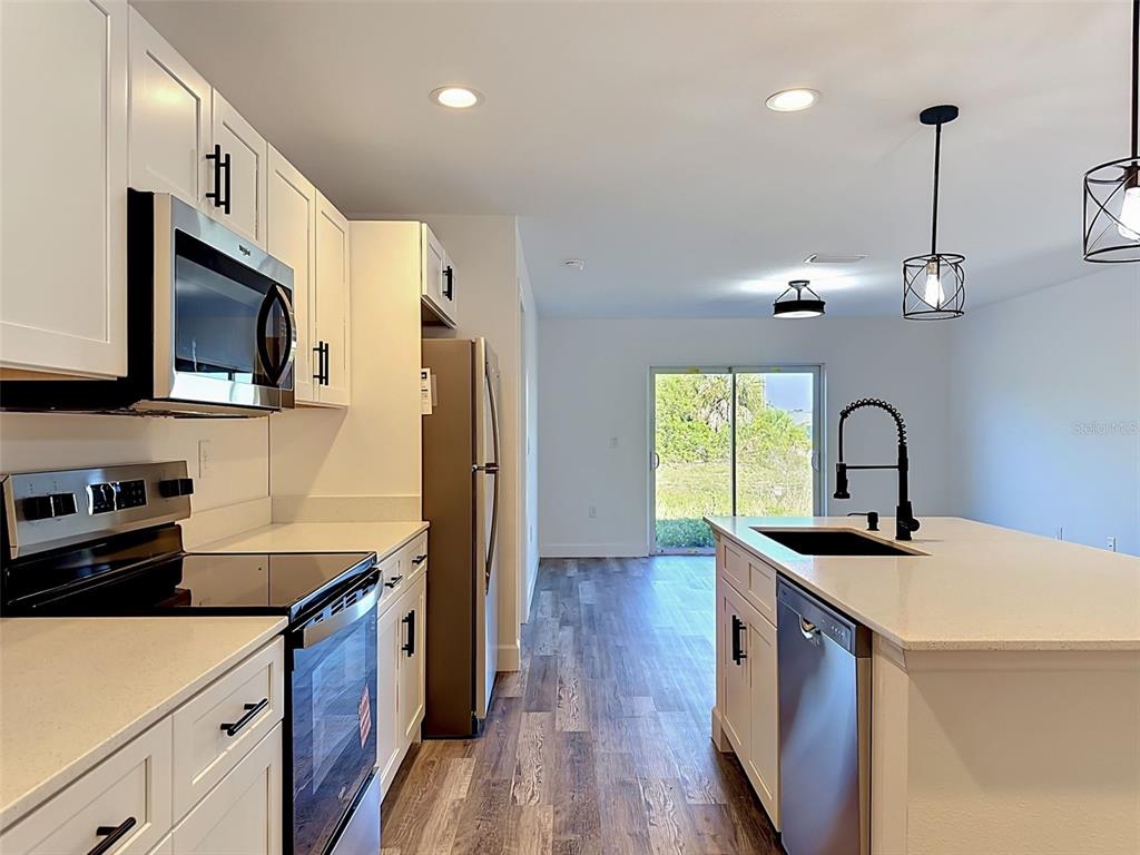 A modern kitchen features white cabinets, stainless steel appliances, a center island, and wood-look flooring — 2715 GISELA RD, NORTH PORT, FL