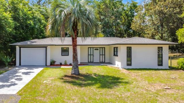 A single-story house with a white exterior, dark window frames, and a palm tree — 47 LAKE COURT LOOP, OCALA, FL