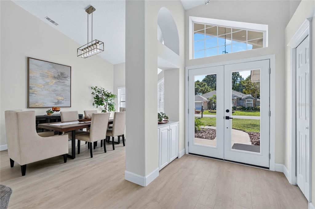 A bright entryway with light wood floors leads into a dining area with modern lighting — 107 LINDSAY DRIVE, PALM COAST, FL