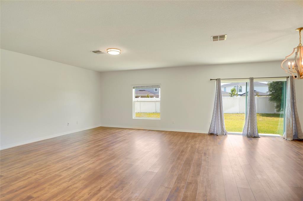 An empty living room features wood-look flooring, white walls, a ceiling light, and sliding glass doors — 3936 FESCUE STREET, CLERMONT, FL