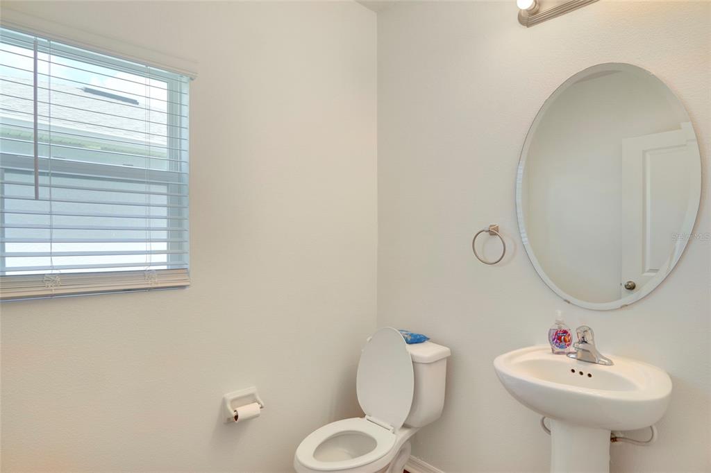 A small bathroom features a pedestal sink, an oval mirror, and a white toilet — 3936 FESCUE STREET, CLERMONT, FL
