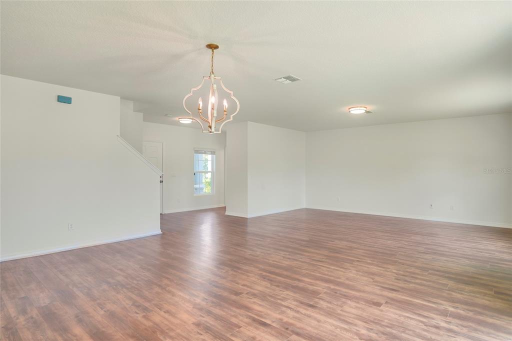 An open-concept living area features light wood-look flooring, white walls, and a decorative chandelier — 3936 FESCUE STREET, CLERMONT, FL