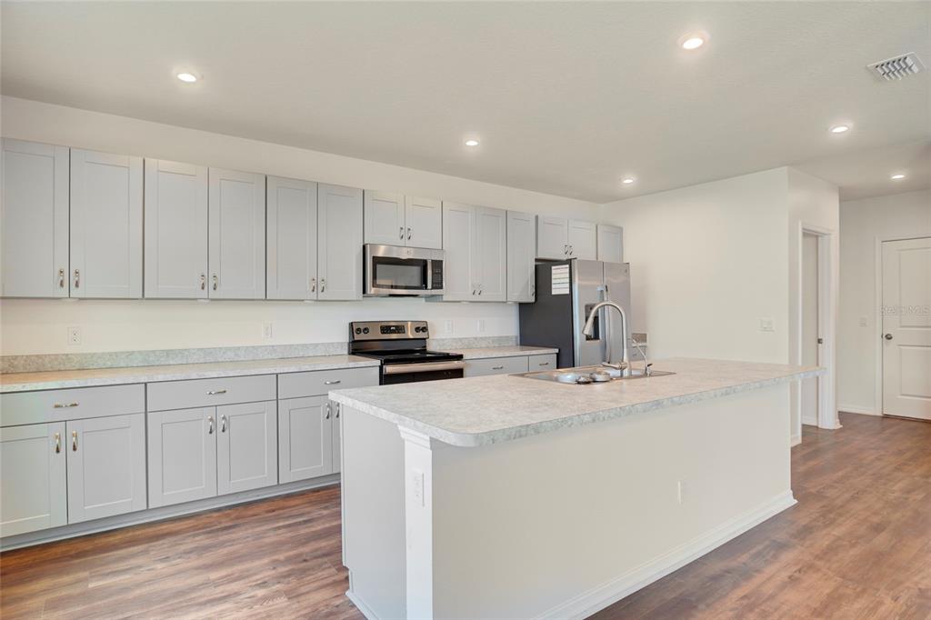 A kitchen features light gray cabinets, stainless steel appliances, and a central island with countertops — 3936 FESCUE STREET, CLERMONT, FL