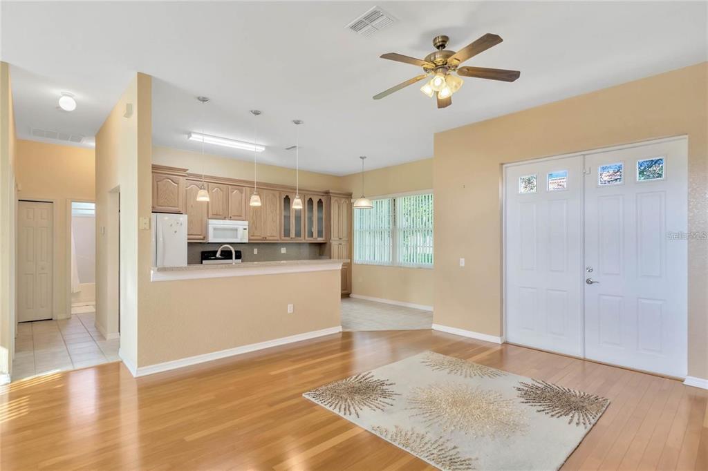 An open-concept living area features hardwood floors, a kitchen with light wood cabinets, and double doors — 503 ANISE COURT, KISSIMMEE, FL