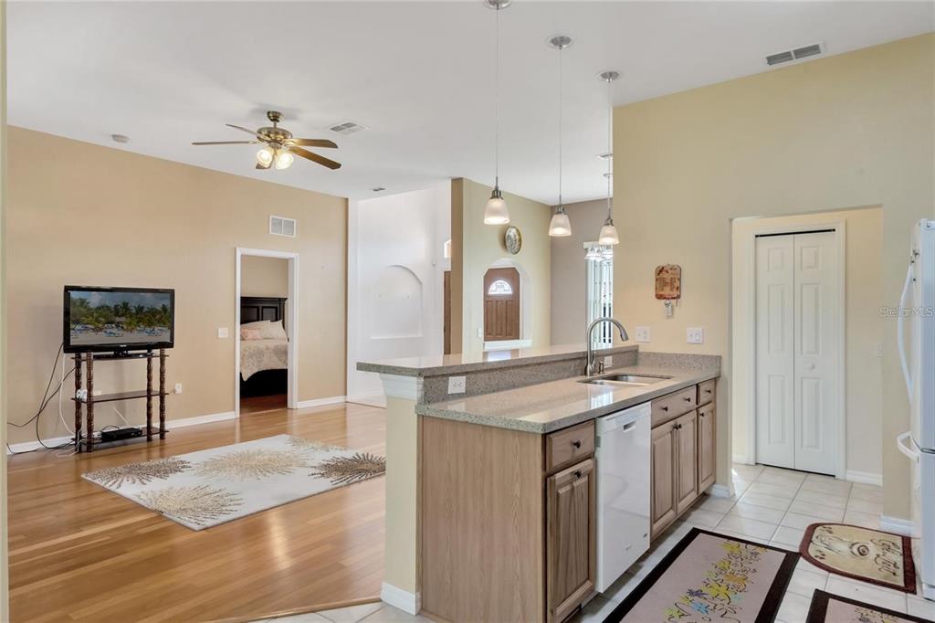 A kitchen with wood cabinets and granite countertops overlooks a living room with hardwood floors — 503 ANISE COURT, KISSIMMEE, FL