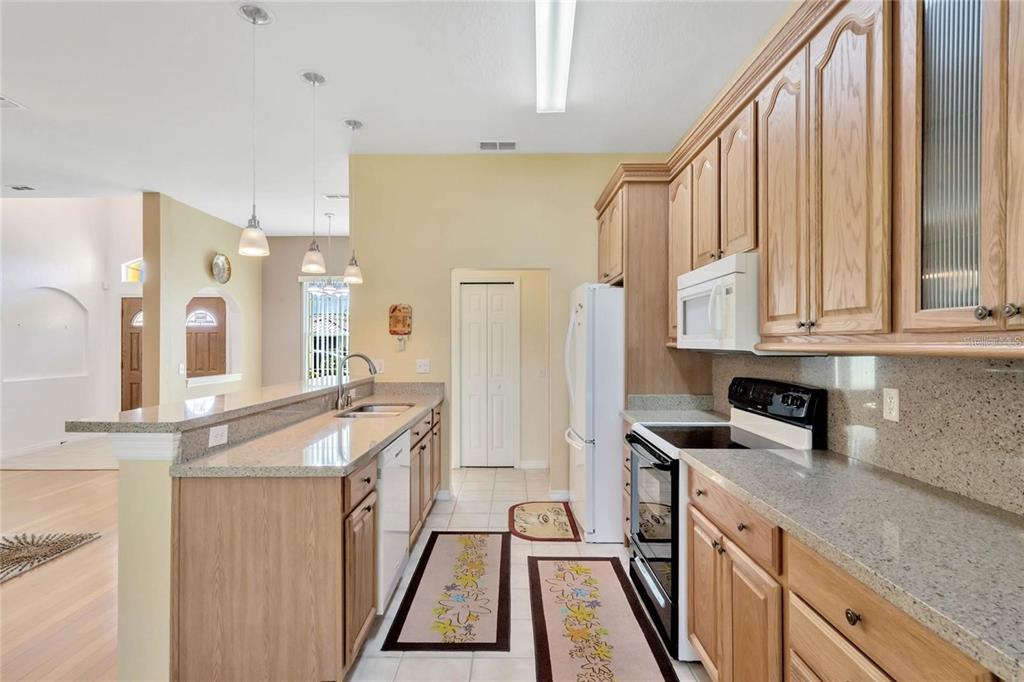 A kitchen features light wood cabinets, granite countertops, white appliances, and a breakfast bar — 503 ANISE COURT, KISSIMMEE, FL