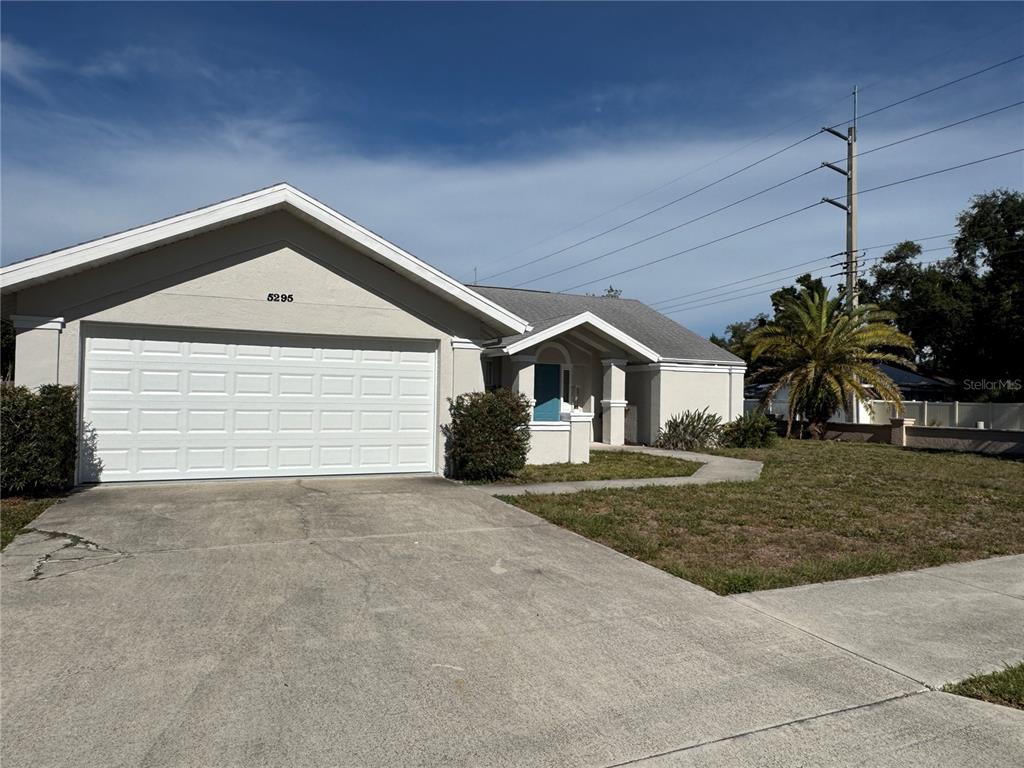A single-story house with a white garage door, beige stucco exterior, and a palm tree — 5295 ASHTON PINES LANE, SARASOTA, FL