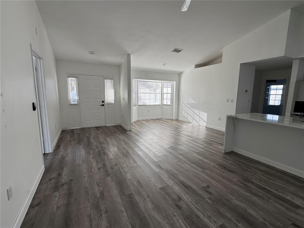 An open-concept living area features gray wood-look flooring, white walls, and a front entryway — 5295 ASHTON PINES LANE, SARASOTA, FL