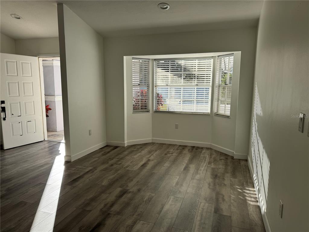An empty room with wood-look flooring, white walls, and a bay window with blinds — 5295 ASHTON PINES LANE, SARASOTA, FL