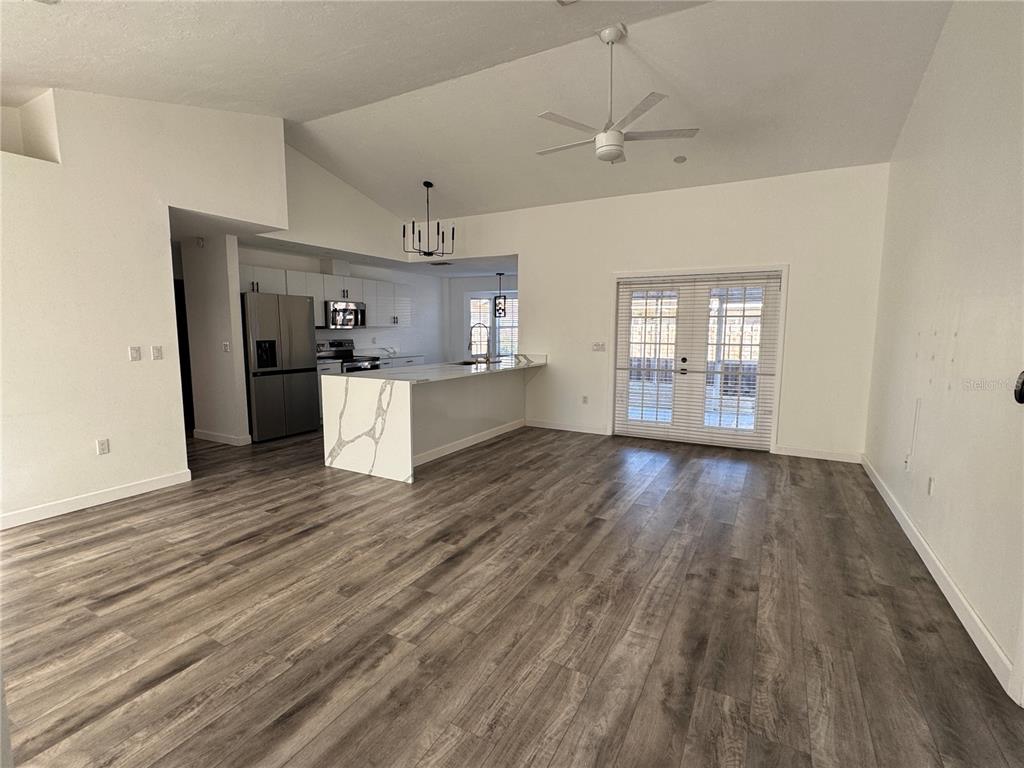An open-concept living area features wood-look flooring, a kitchen with white cabinets, and French doors — 5295 ASHTON PINES LANE, SARASOTA, FL