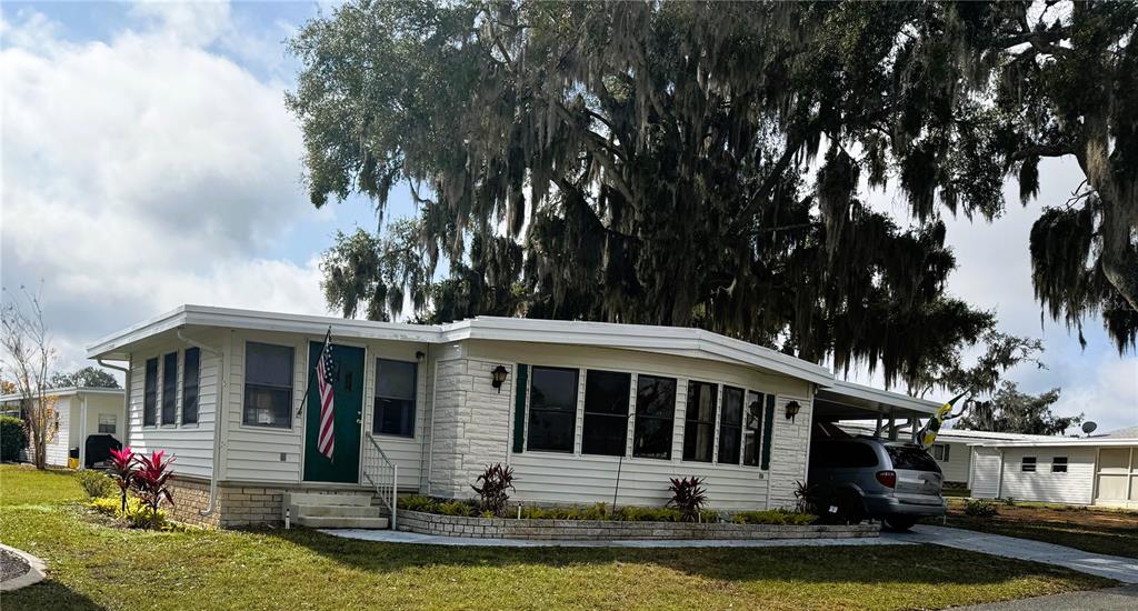 A single-story mobile home with white siding, a green front door, and a carport — 407 PALO VERDE DRIVE, LEESBURG, FL