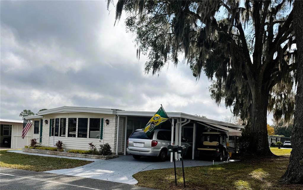 A single-story manufactured home with a carport, a golf cart, and a large oak tree — 407 PALO VERDE DRIVE, LEESBURG, FL
