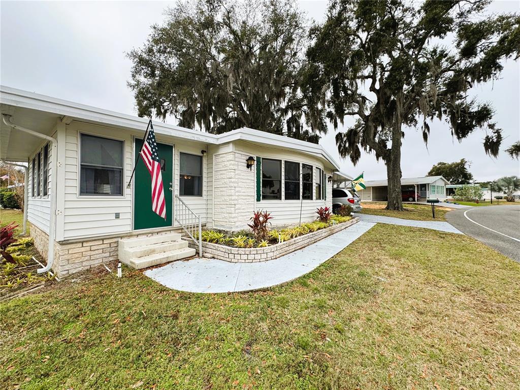 A single-story mobile home with white siding, a green door, and a brick-bordered garden bed — 407 PALO VERDE DRIVE, LEESBURG, FL