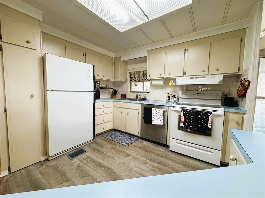 A kitchen features light-colored cabinets, a white refrigerator, a stainless dishwasher, and a white stove — 407 PALO VERDE DRIVE, LEESBURG, FL