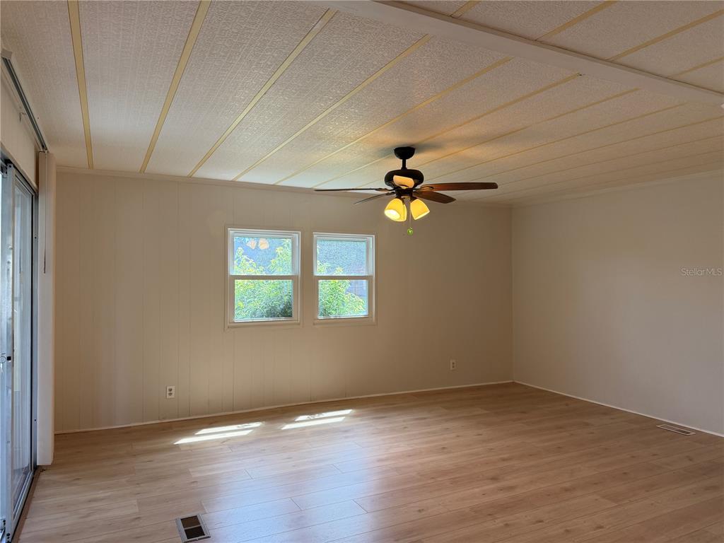 An empty living room features light wood-look flooring, white paneled walls, and a ceiling fan — 925 BEECHWOOD AVENUE, LADY LAKE, FL