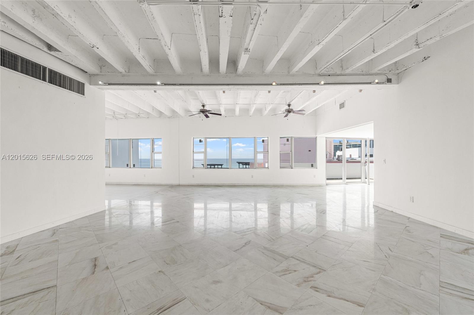 A spacious, white-walled room features marble floors, exposed ceiling beams, and large windows overlooking the ocean — 5255 Collins Ave, Miami Beach FL 33140, MIAMI BEACH, FL