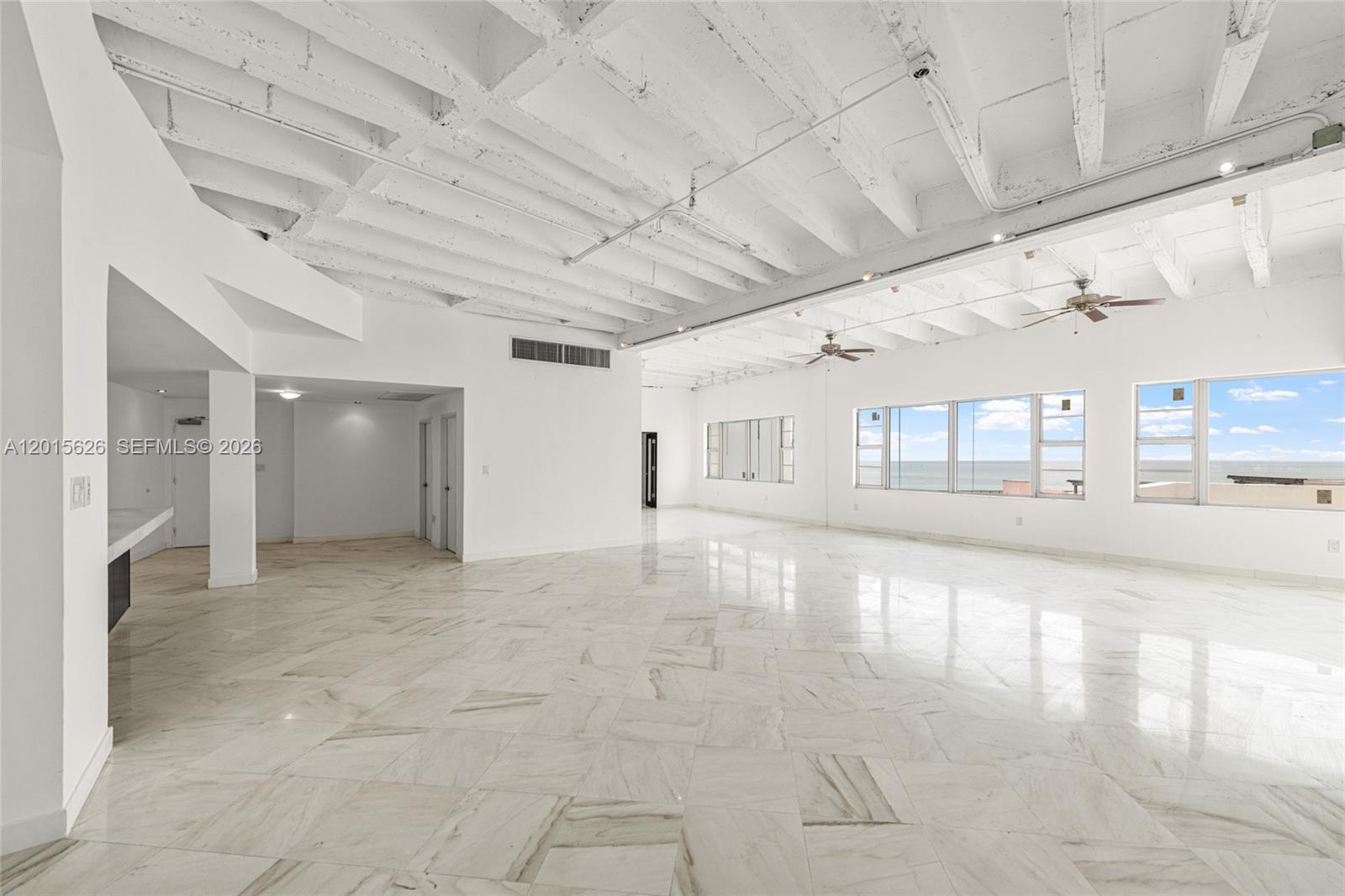 A spacious, open-concept room features white marble floors, exposed white ceiling beams, and ocean views — 5255 Collins Ave, Miami Beach FL 33140, MIAMI BEACH, FL