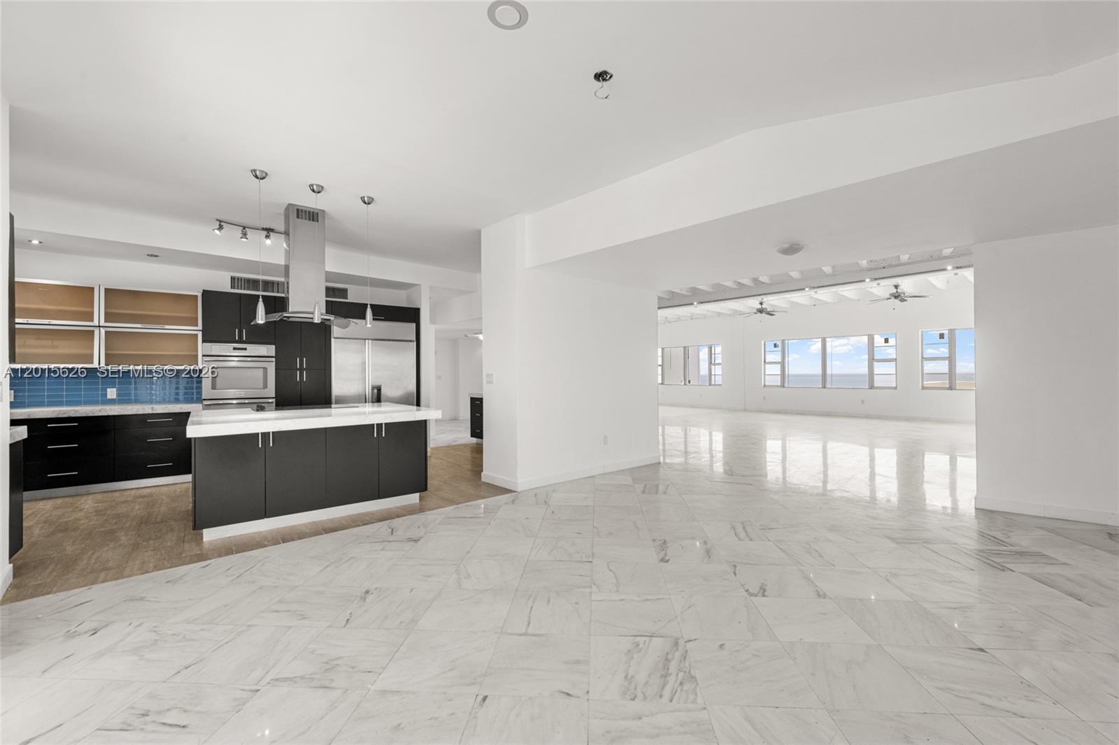 A modern kitchen with dark cabinetry and a white island opens to a large room — 5255 Collins Ave, Miami Beach FL 33140, MIAMI BEACH, FL