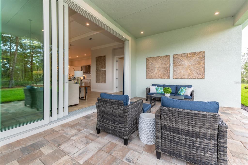A covered patio features wicker furniture, a stone paver floor, and large sliding glass doors — 1631 LAKE RESERVE DRIVE, DELAND, FL