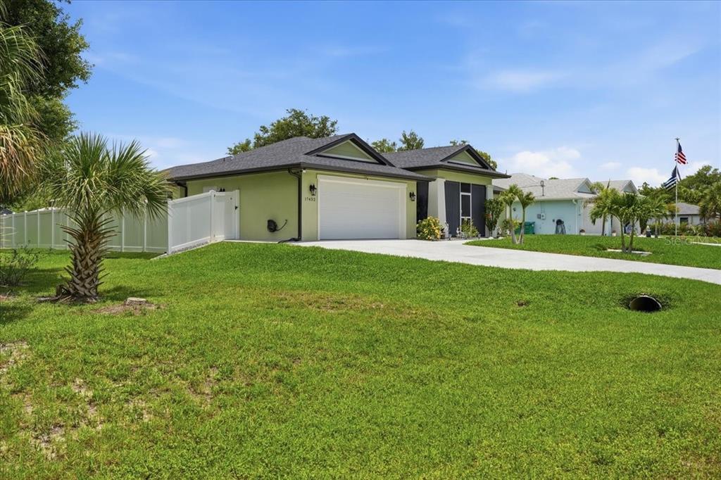 A light green single-story house with a two-car garage and a white vinyl fence — 17432 SHIRLEY AVENUE, PORT CHARLOTTE, FL