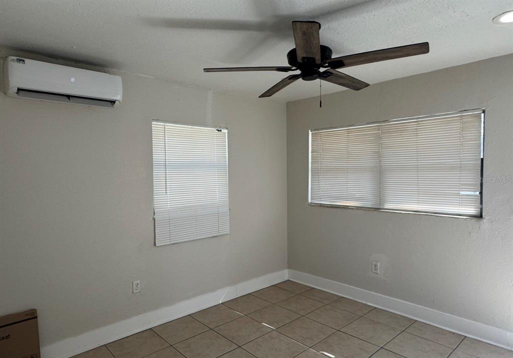 An empty room features tile flooring, a ceiling fan, and a wall-mounted air conditioning unit — 10022 N LANTANA AVENUE UNIT A, TAMPA, FL