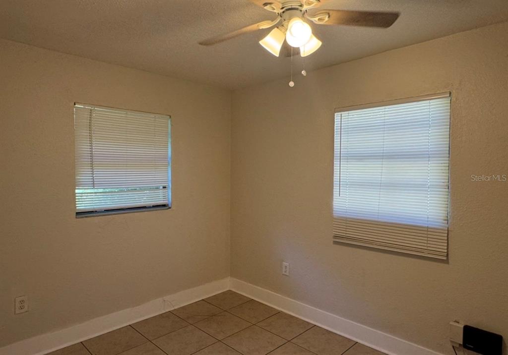 An empty bedroom features beige walls, tile flooring, a ceiling fan, and two windows — 10022 N LANTANA AVENUE UNIT A, TAMPA, FL